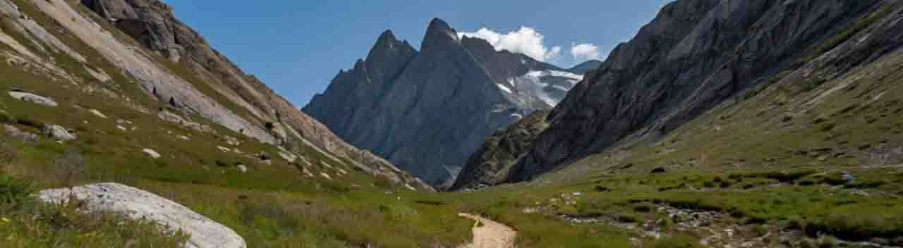 Ein Pfad, der sich durch Gras und Felsen schlängelt und zu einer Gebirgskette führt, die im Hintergrund zu sehen ist.