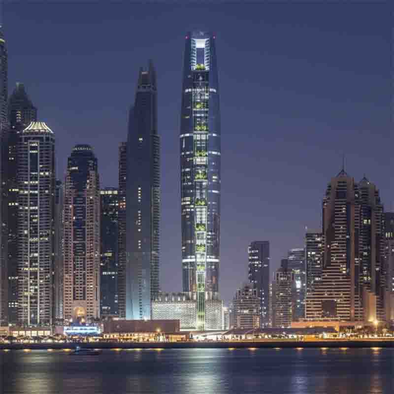 Die beleuchtete Skyline von Dubai Marina bei Nacht, aufgenommen über dem Wasser, wobei Ciel Dubai Marina, das höchste Hotel der Welt im Zentrum der Szene steht.