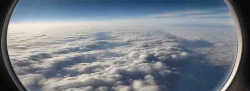 Blick aus dem Flugzeugfenster auf einen klaren blauen Himmel mit weißen Schäfchenwolken.