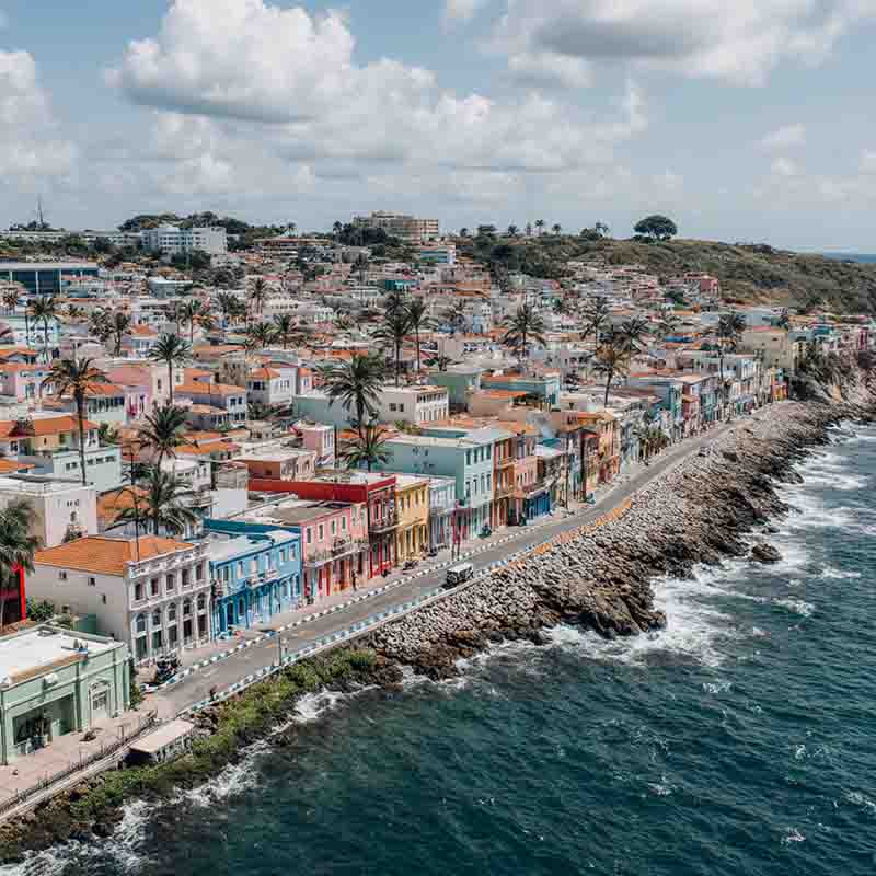 Panoramablick auf die Küstenlinie von San Juan, Puerto Rico, mit einer Reihe bunter Gebäude entlang des felsigen Ufers und Palmen, die unter einem teilweise bewölkten Himmel wachsen.