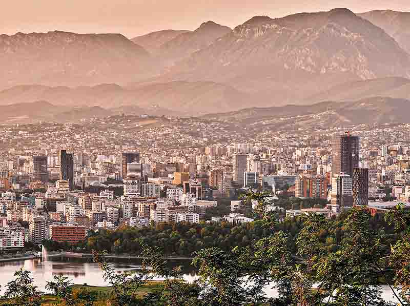 Blick auf die Skyline von Tirana in der Abenddämmerung von der südlichen Seite, mit dem Skanderbeg-Gebirge im Hintergrund