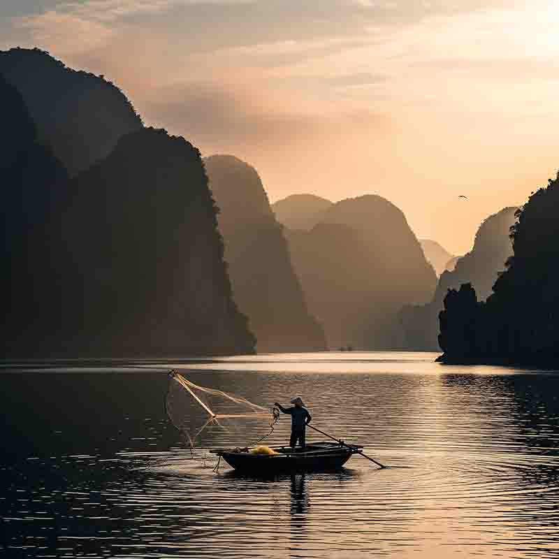 Ein Fischer in einem Boot wirft sein Netz bei Sonnenaufgang vor der Kulisse der Kalksteininseln der Ha Long Bucht.